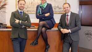 Three people standing in a reception area with a wooden desk and a framed picture on the wall. - Hotel Gollner (Graz)