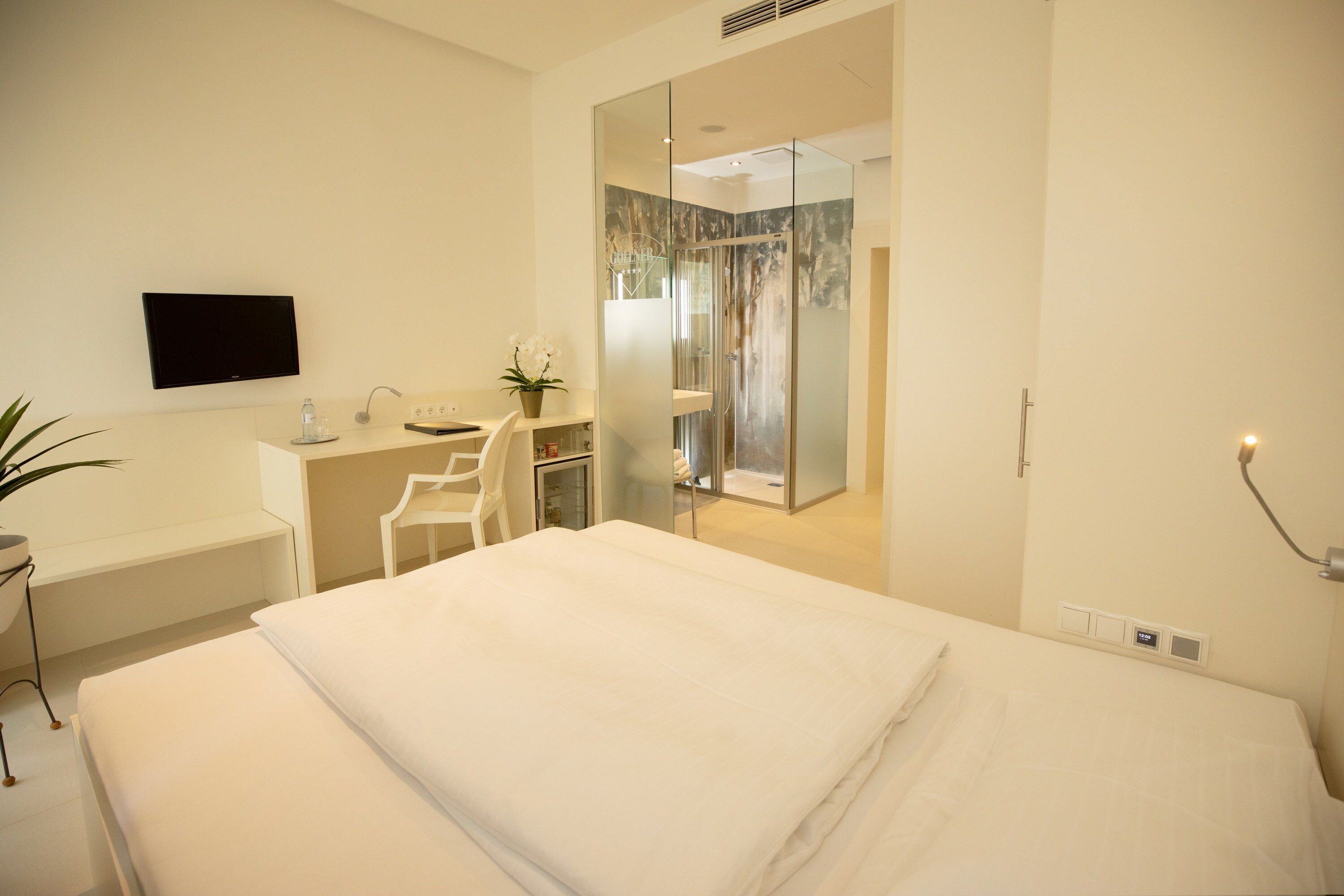 Una habitación de hotel moderna con cama, escritorio, silla, televisor y zona de ducha.
