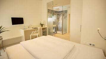 A modern hotel room with a bed, a desk, a chair, a TV, and a shower area.