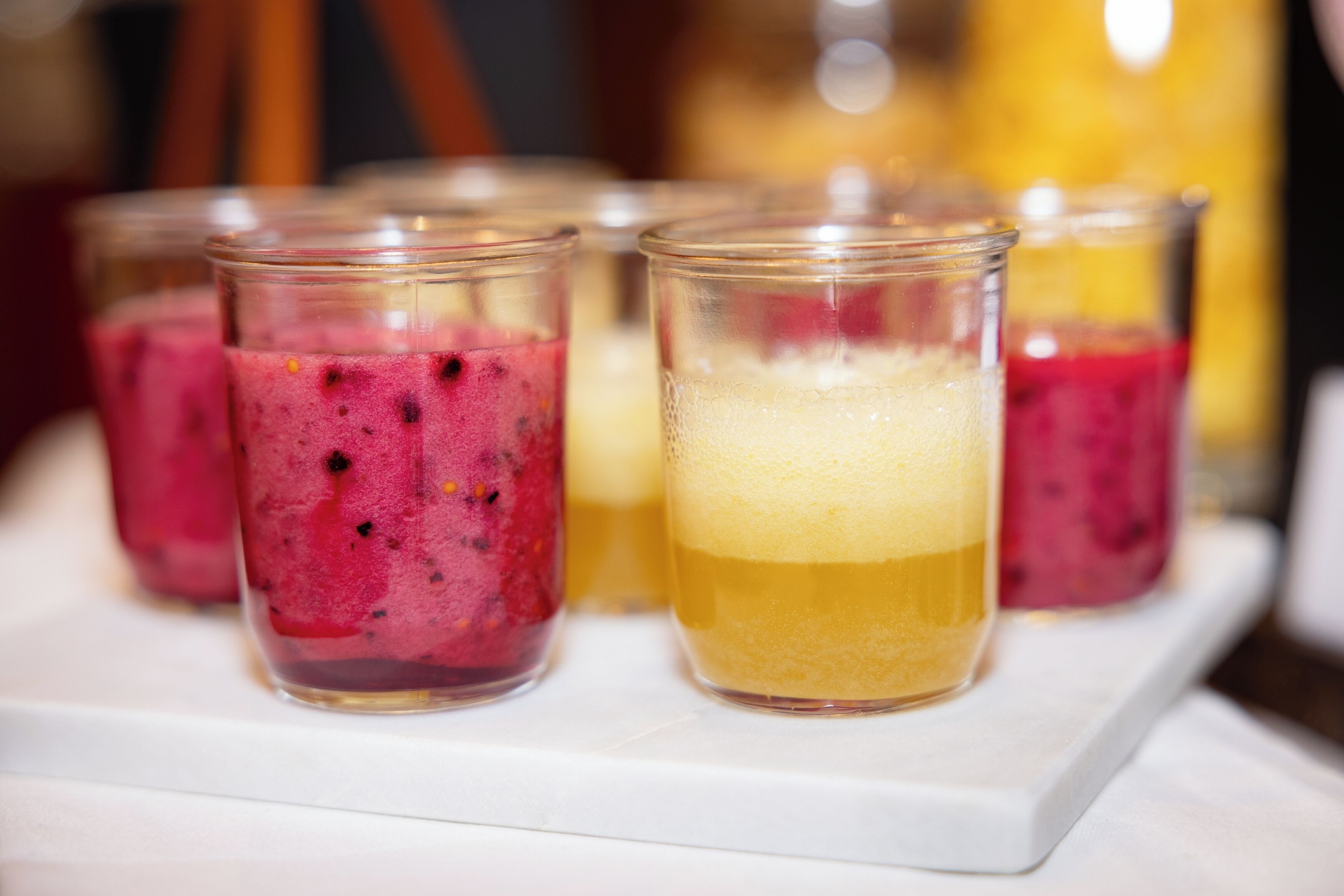 Four glasses of fruit smoothie on a white tray.