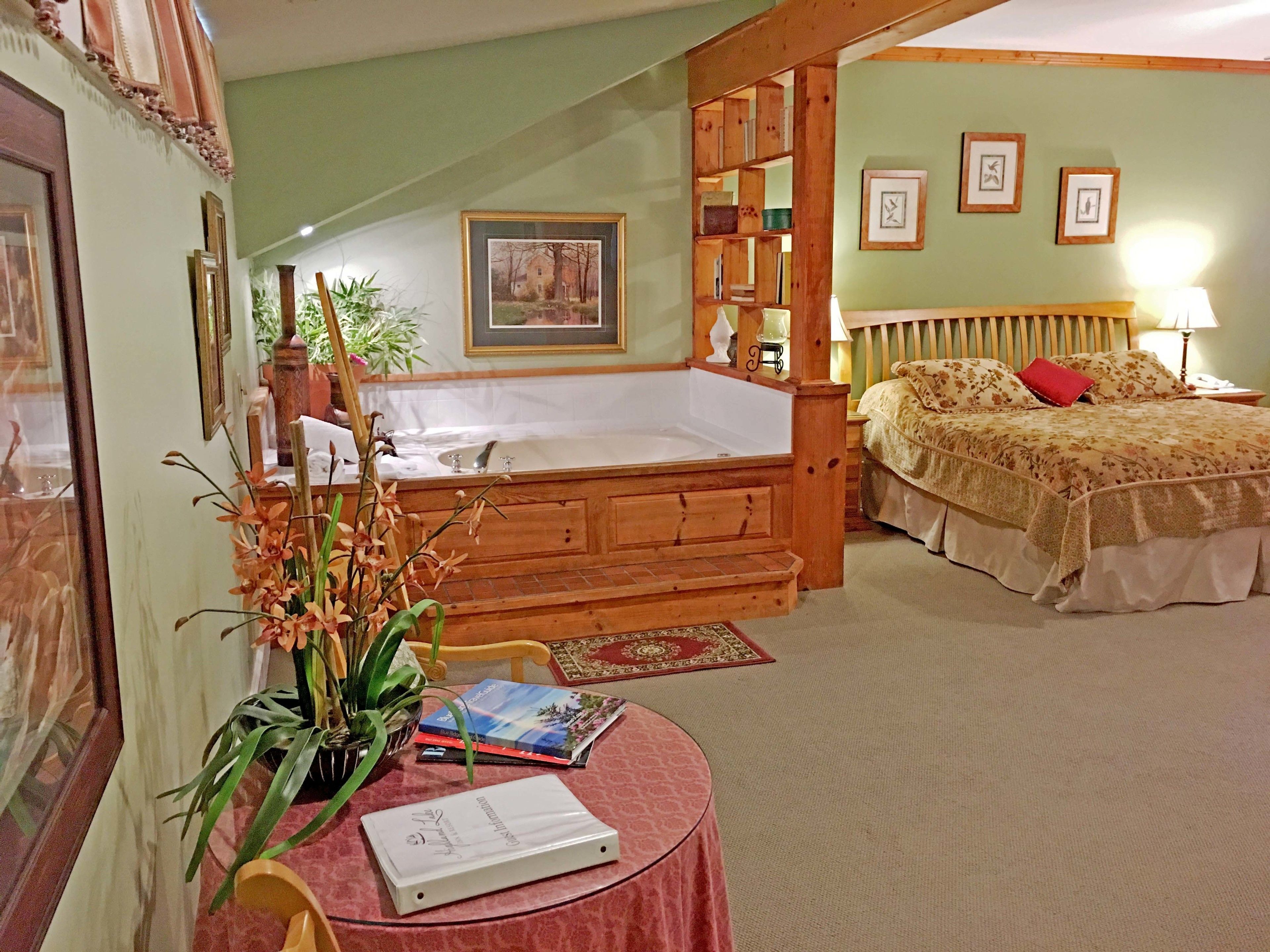 A bedroom with a large bed, a wooden headboard, a nightstand, a lamp, a bookshelf, and a window with a view of a house.