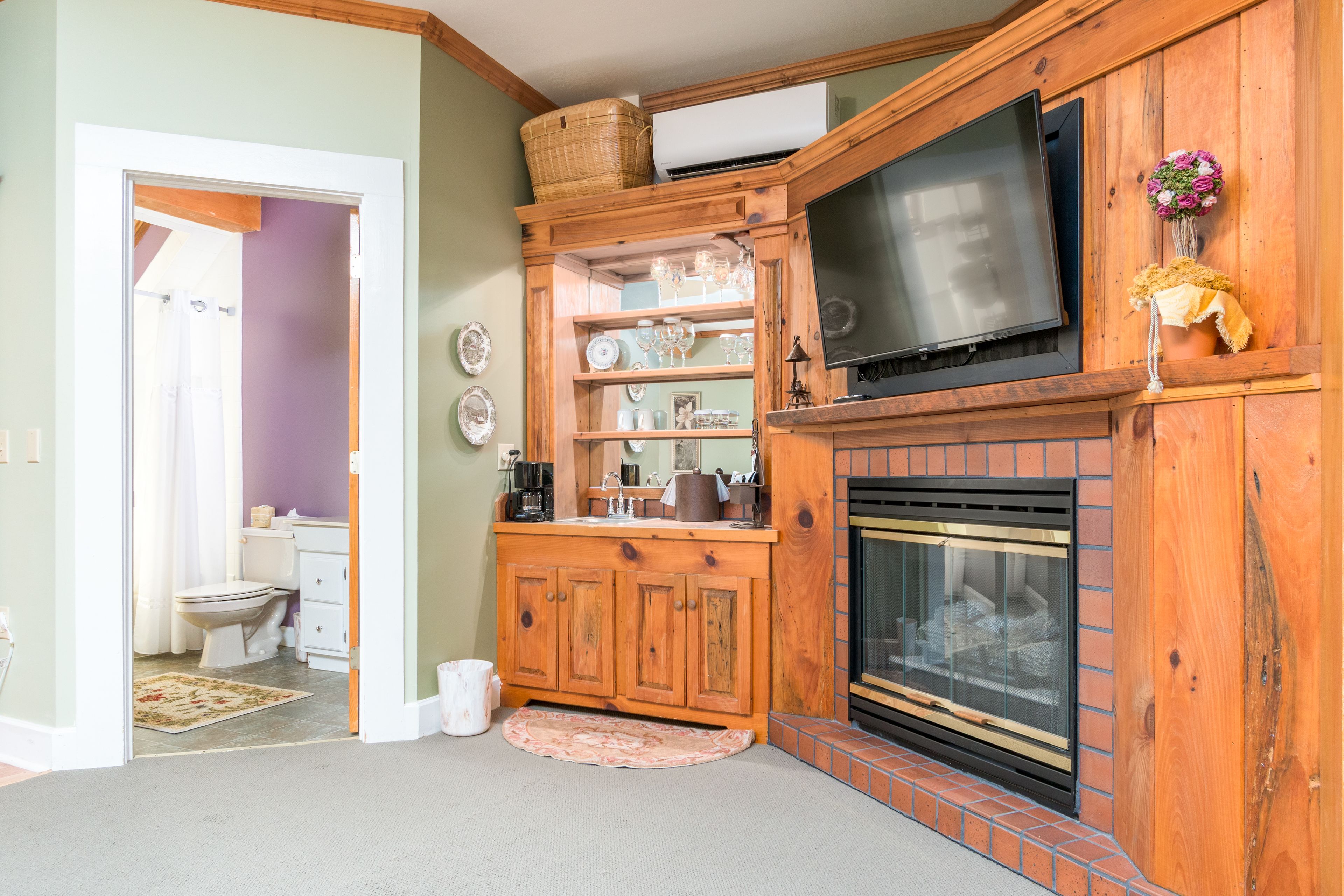 A living room with a fireplace, wooden cabinets, a television, and a bathroom visible through an open door.