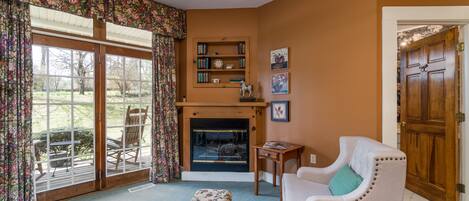 A living room with a fireplace, a bookshelf, a sofa, and a dining area with chairs.
