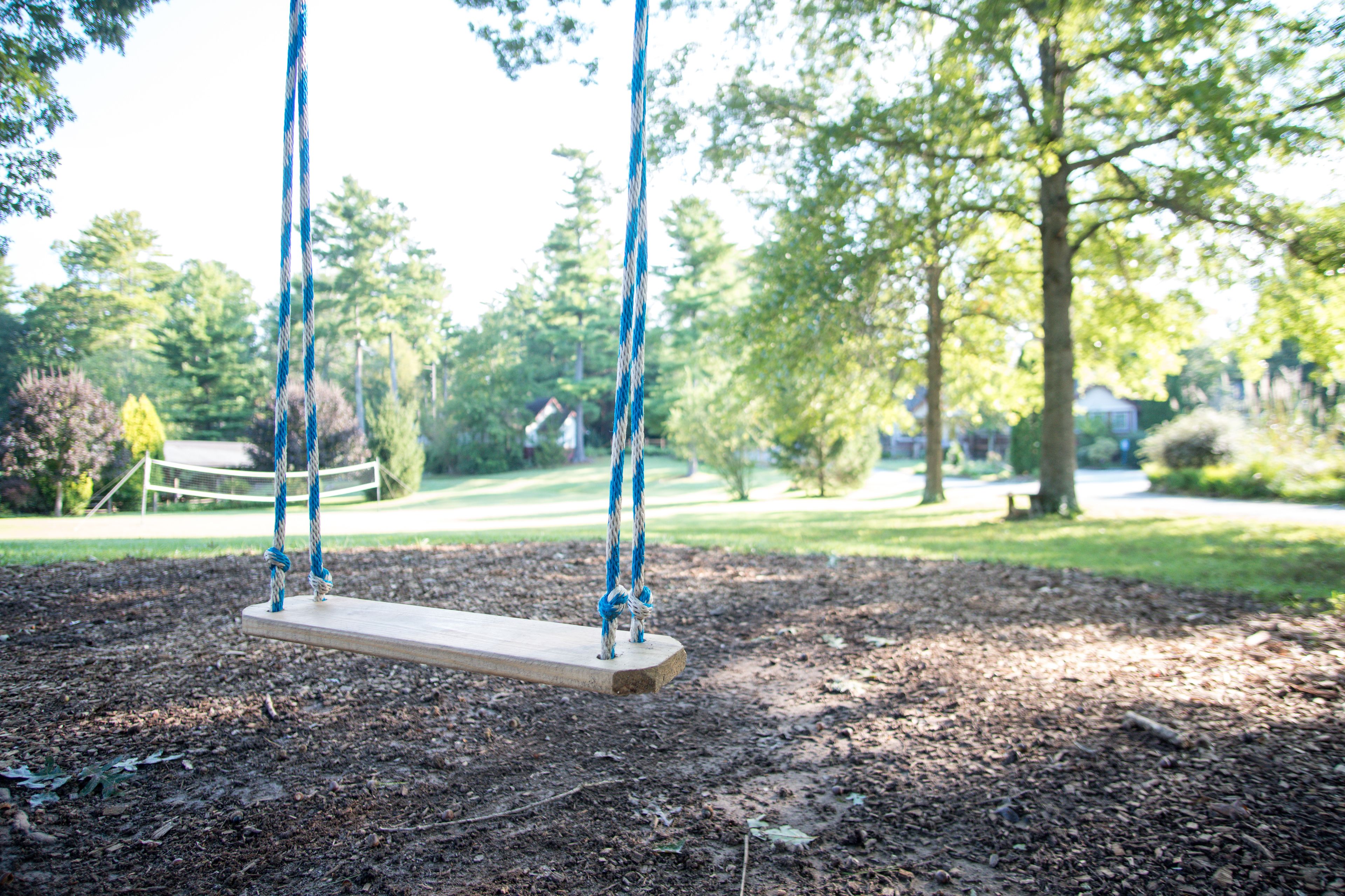 A wooden swing set in a park with ropes, surrounded by trees and a grassy area.