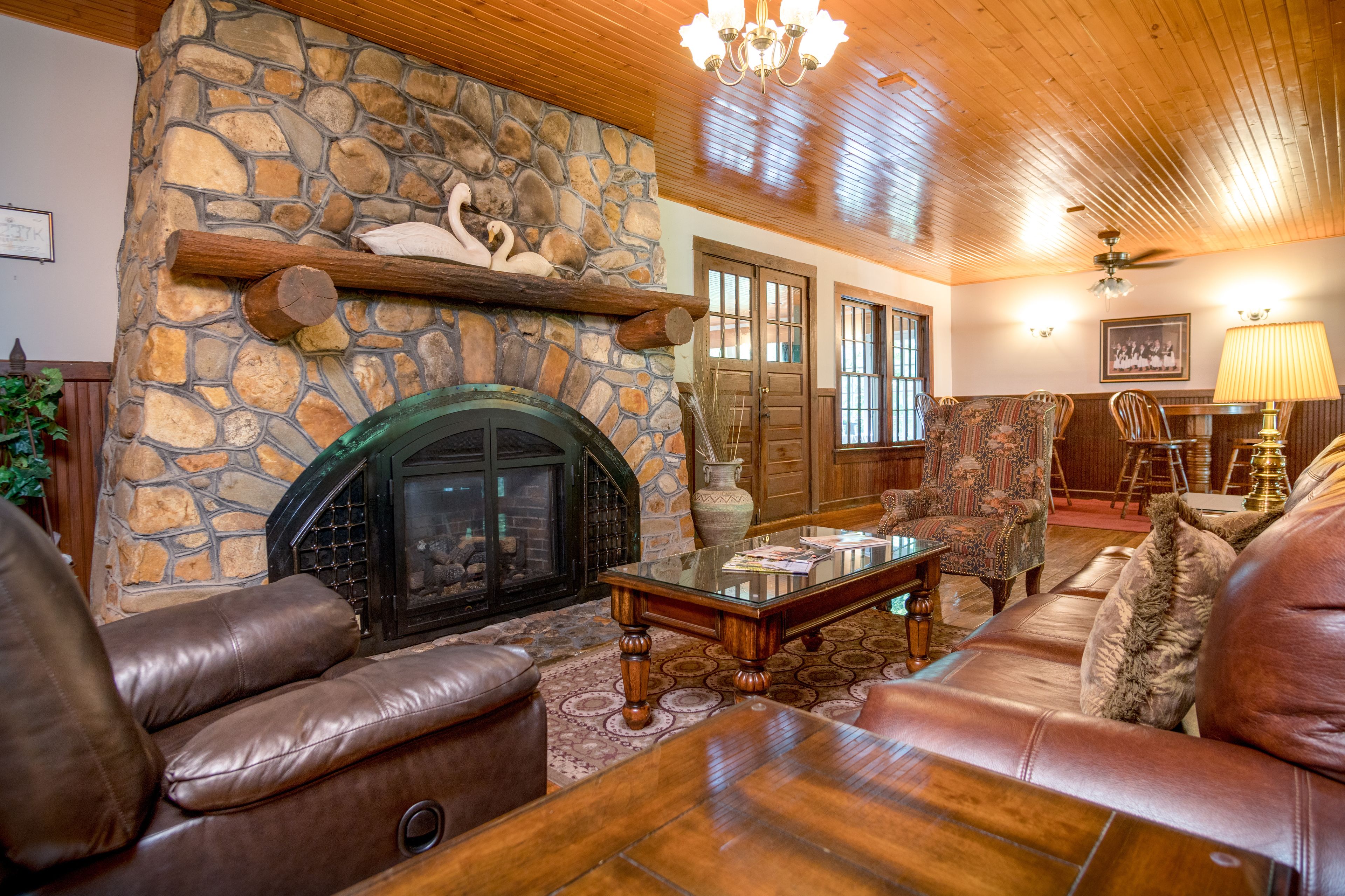 A cozy living room with a stone fireplace, leather sofas, and a wooden ceiling.
