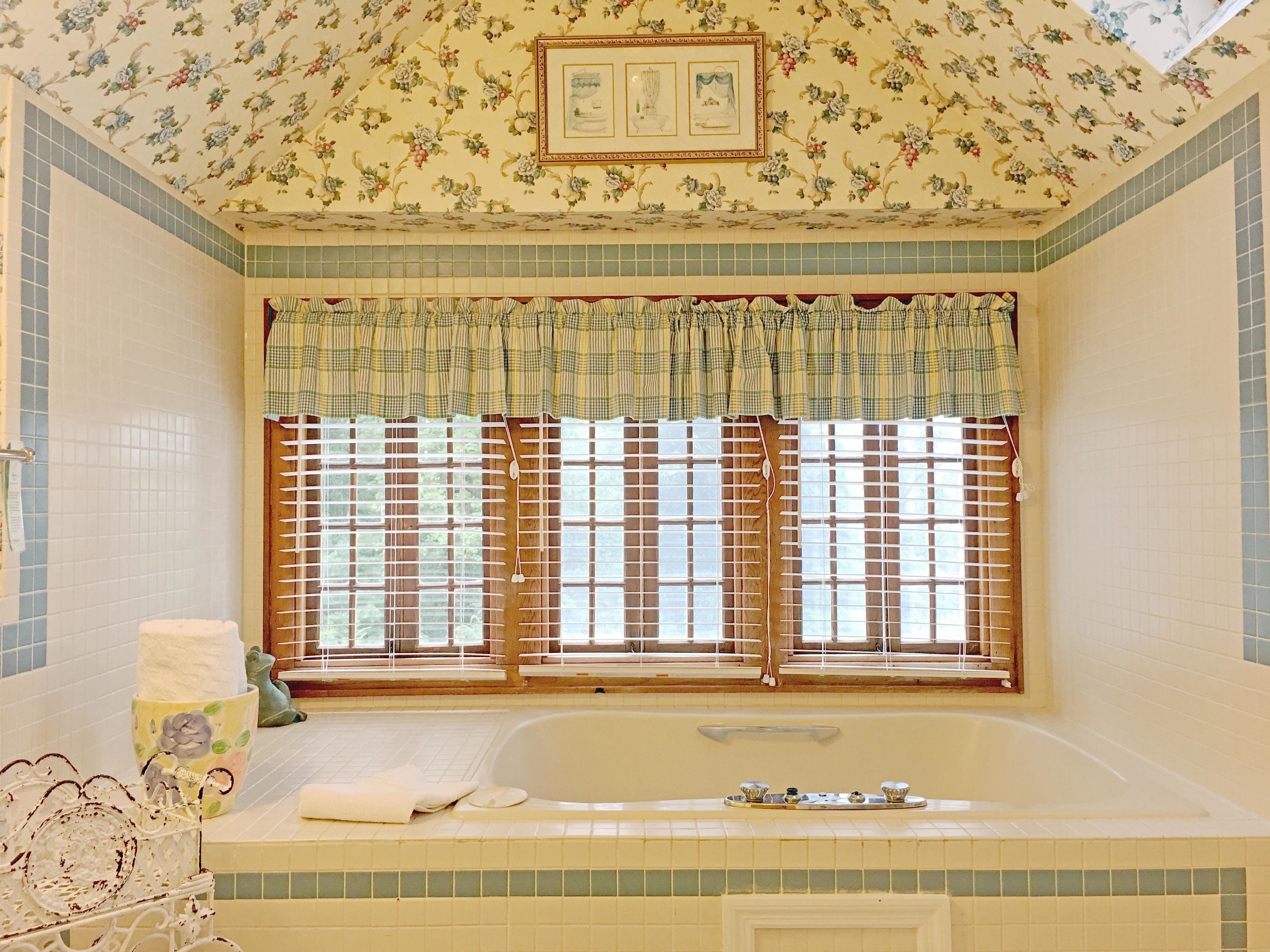 A bathroom with a bathtub, a window with blinds, and a floral ceiling design.