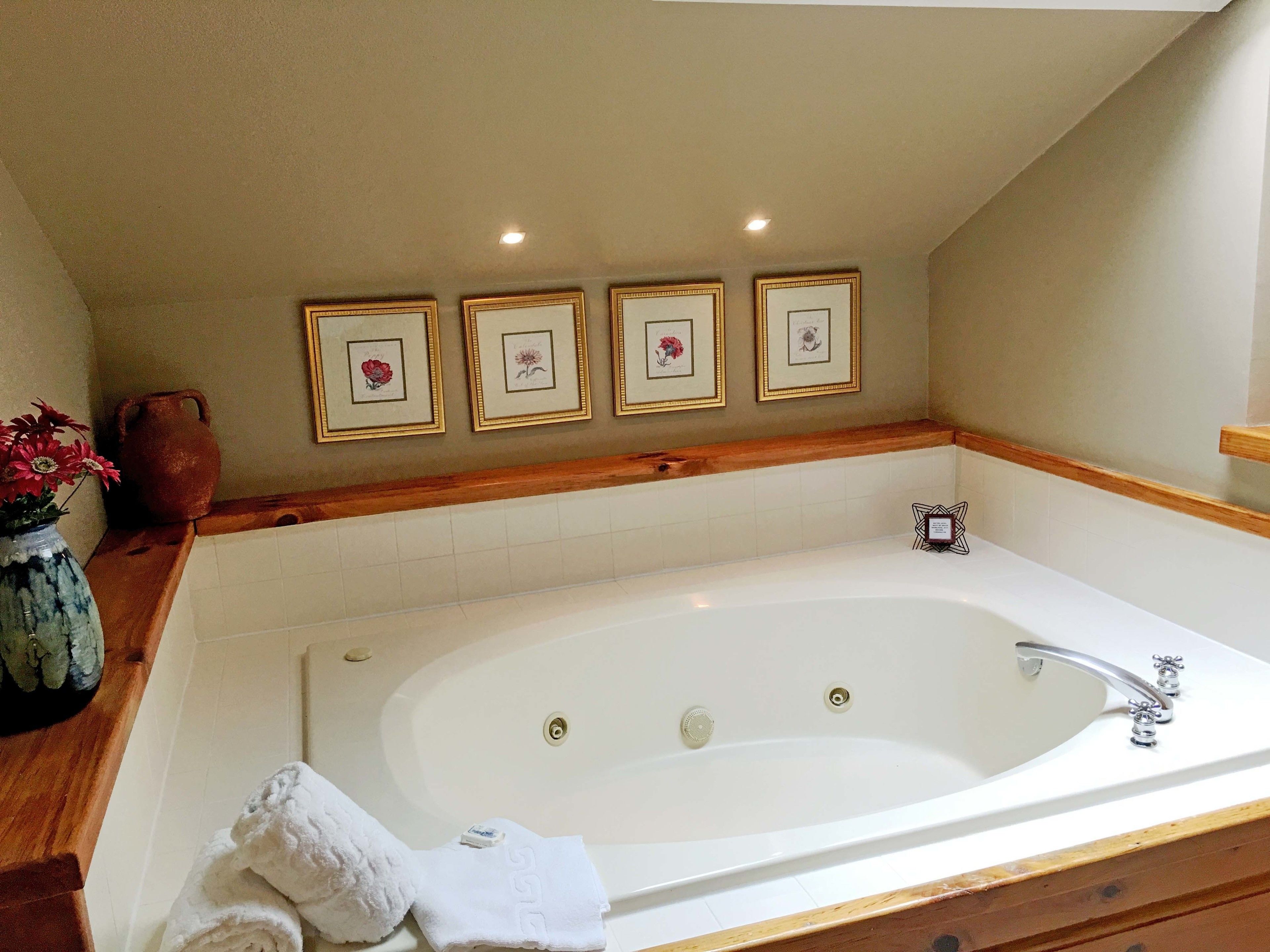 A bathroom with a large bathtub, a wooden vanity, and framed artwork on the wall.