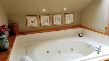 A bathroom with a large bathtub, a wooden vanity, and framed artwork on the wall.