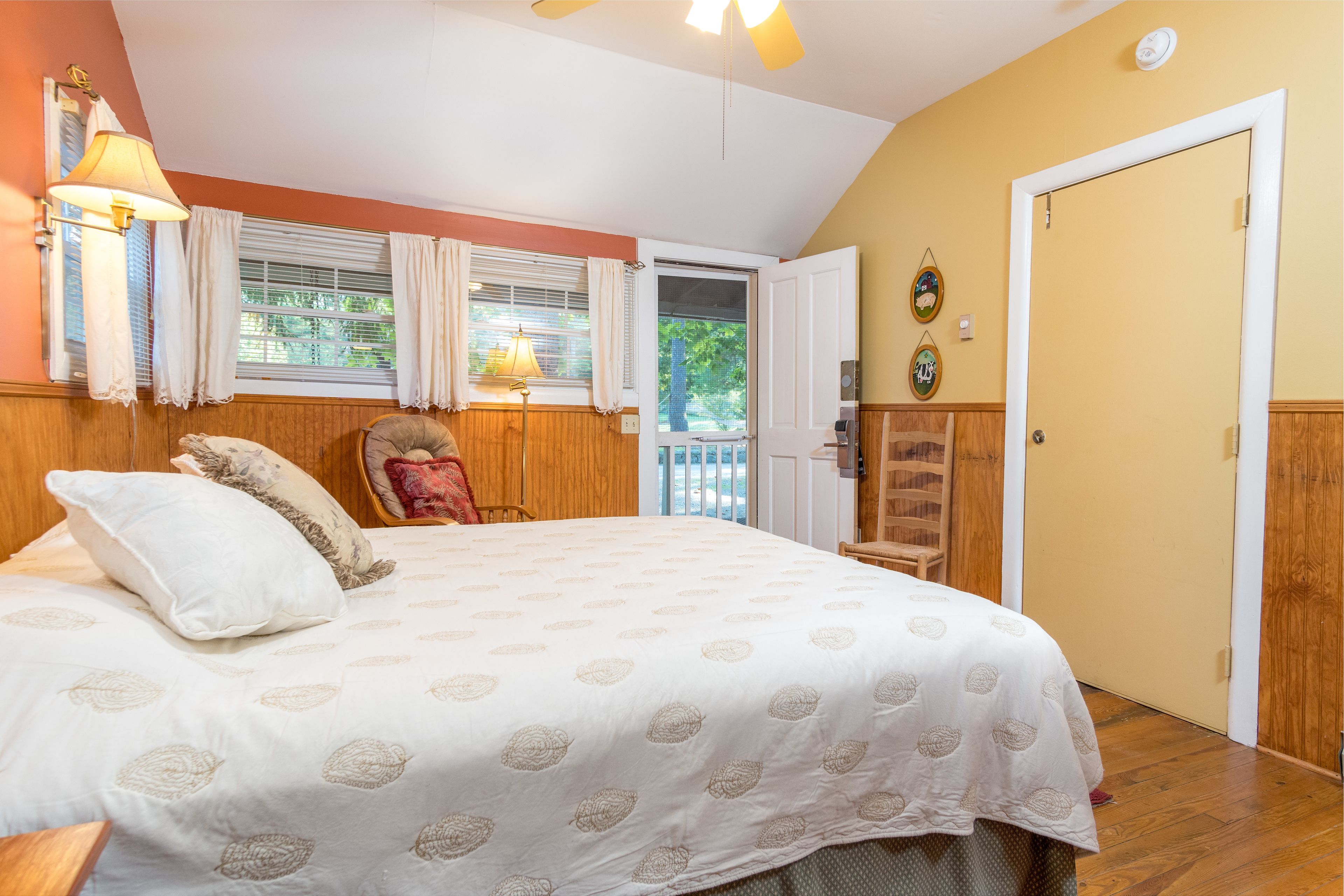 Un dormitorio con una cama grande, una silla, una puerta y una ventana con cortinas.