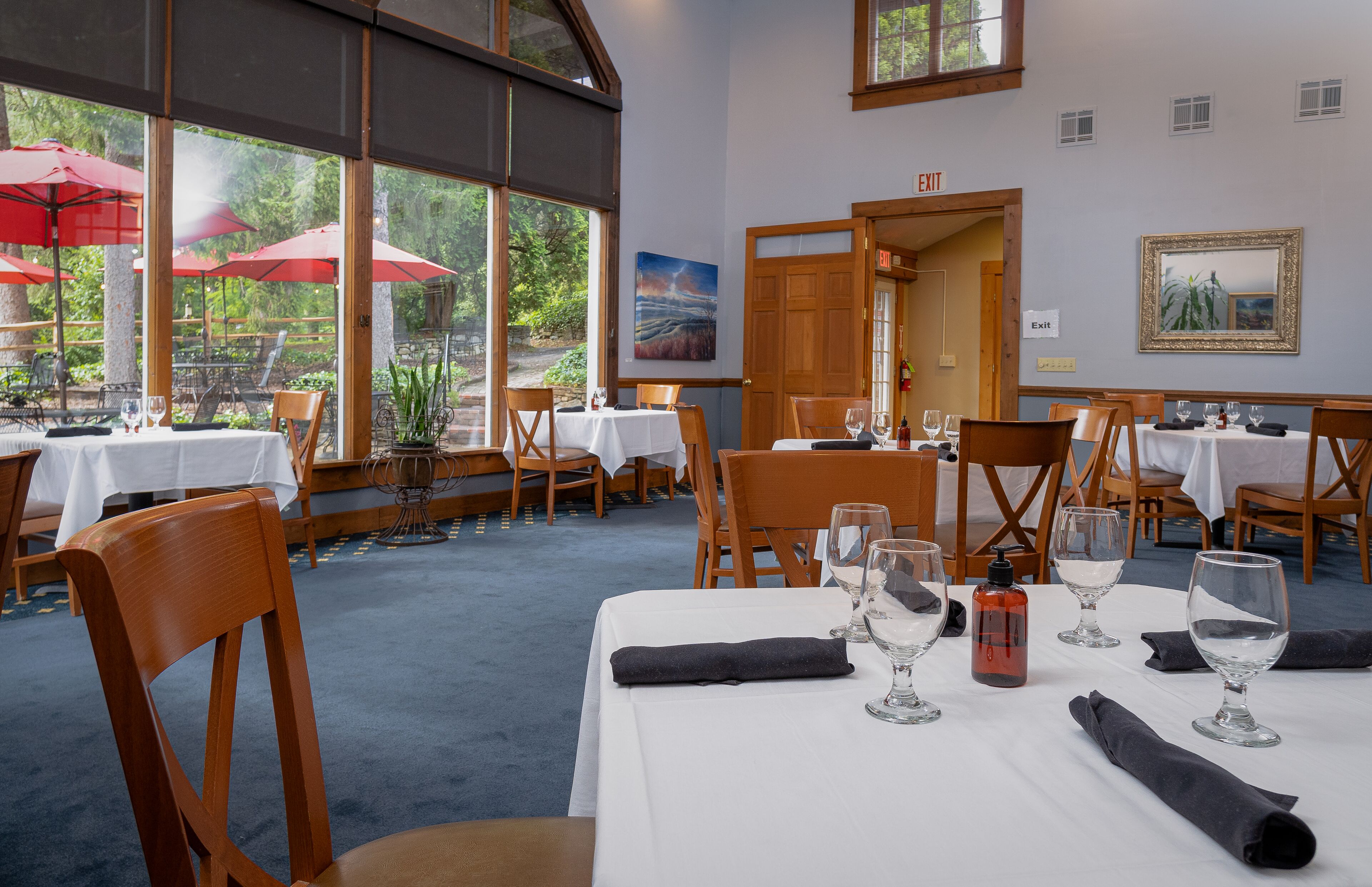 Un restaurante con mesas dispuestas para comer, ventanas amplias y sombrillas exteriores.