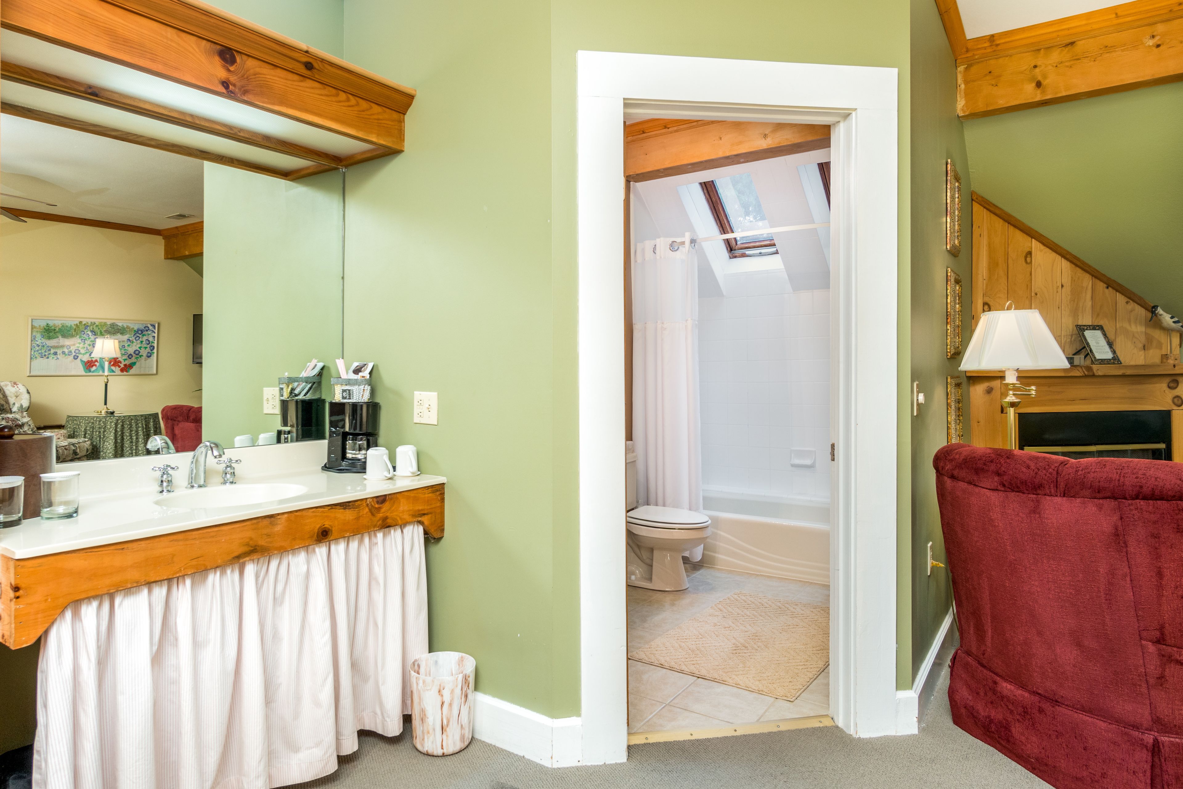 A bathroom with a wooden vanity, a shower, and a red chair.