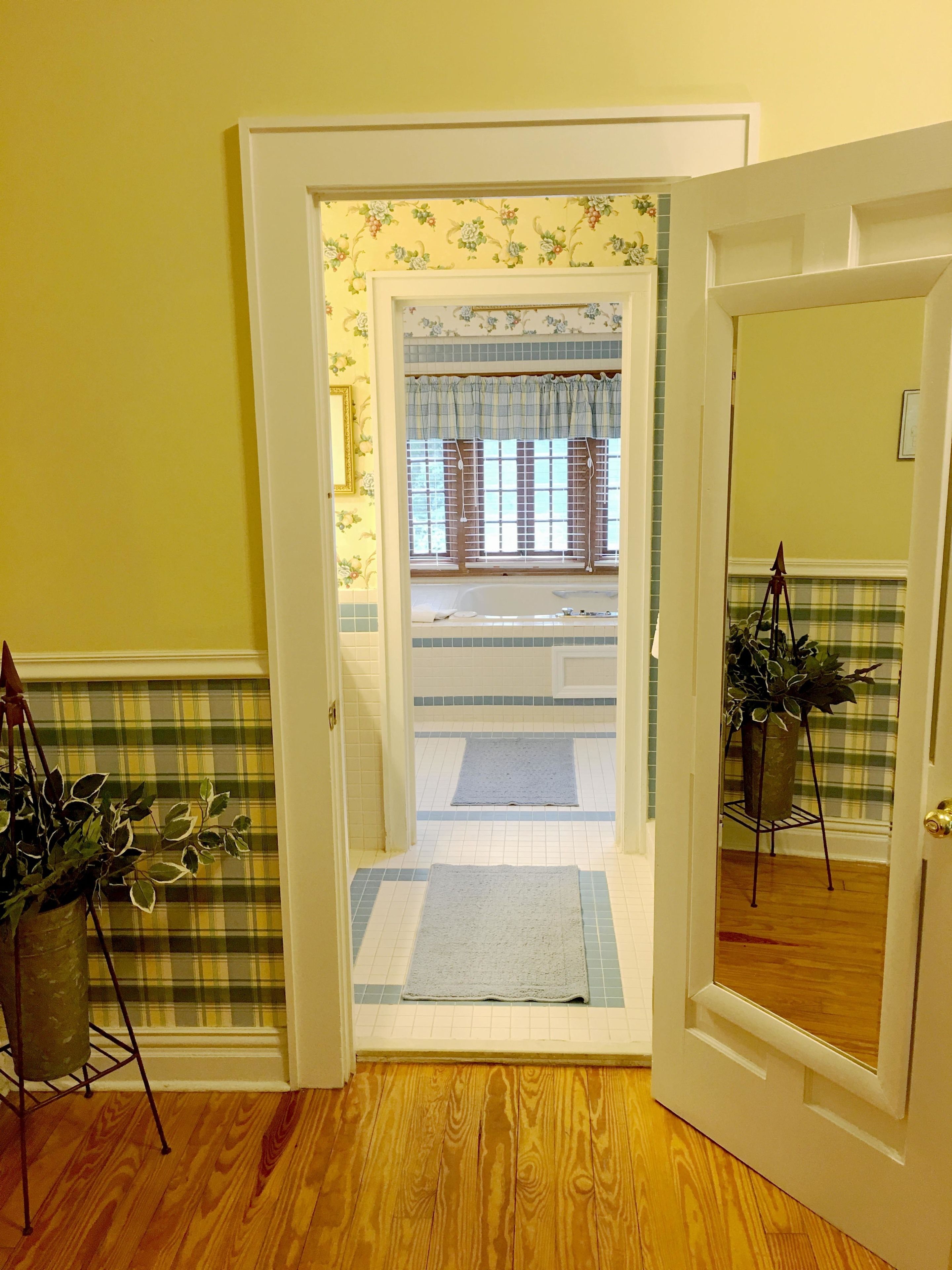 A doorway leading to a room with a checkered floor, a window with curtains, and a potted plant.