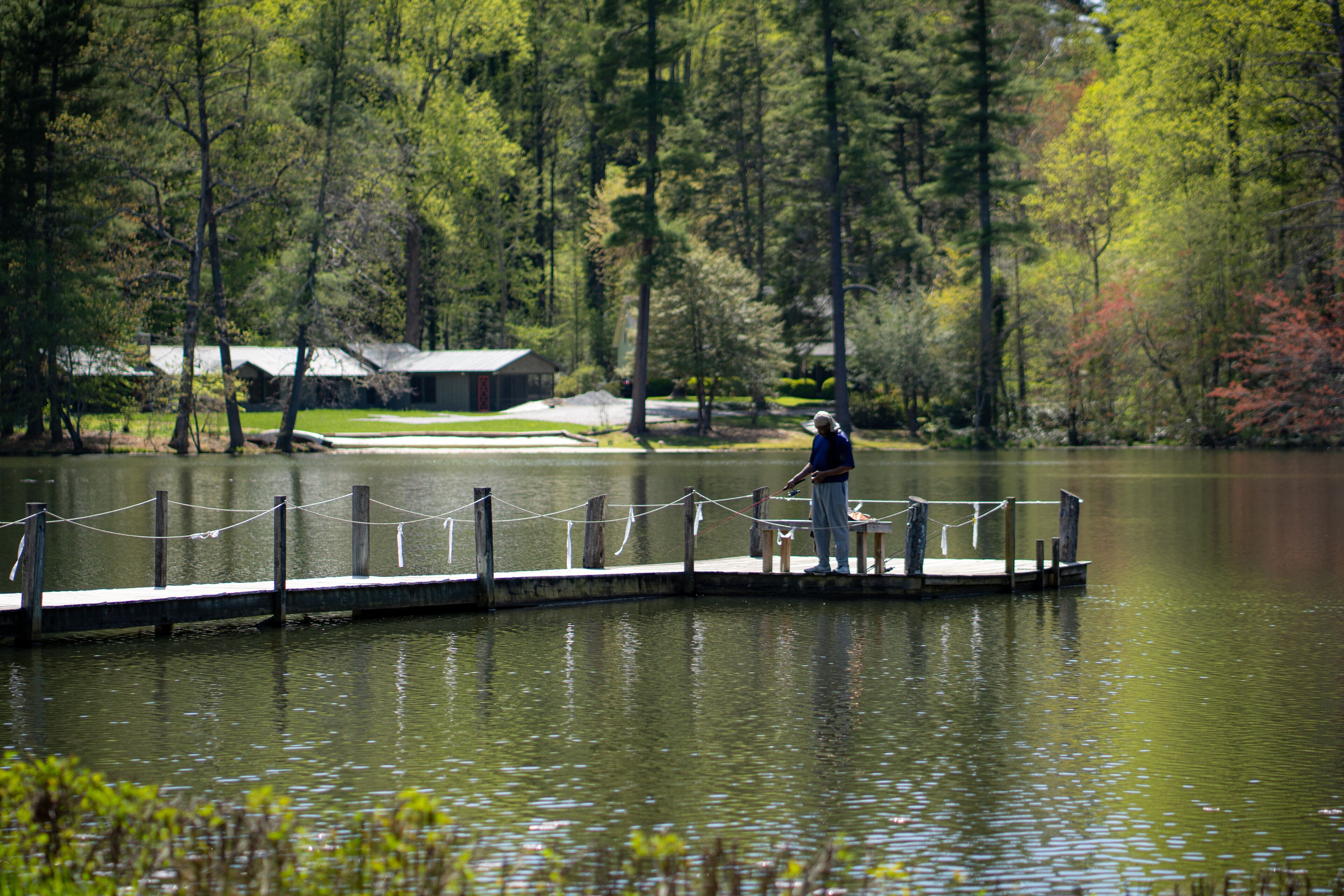 A wooden dock extending into a calm lake, surrounded by trees and a small building in the background.