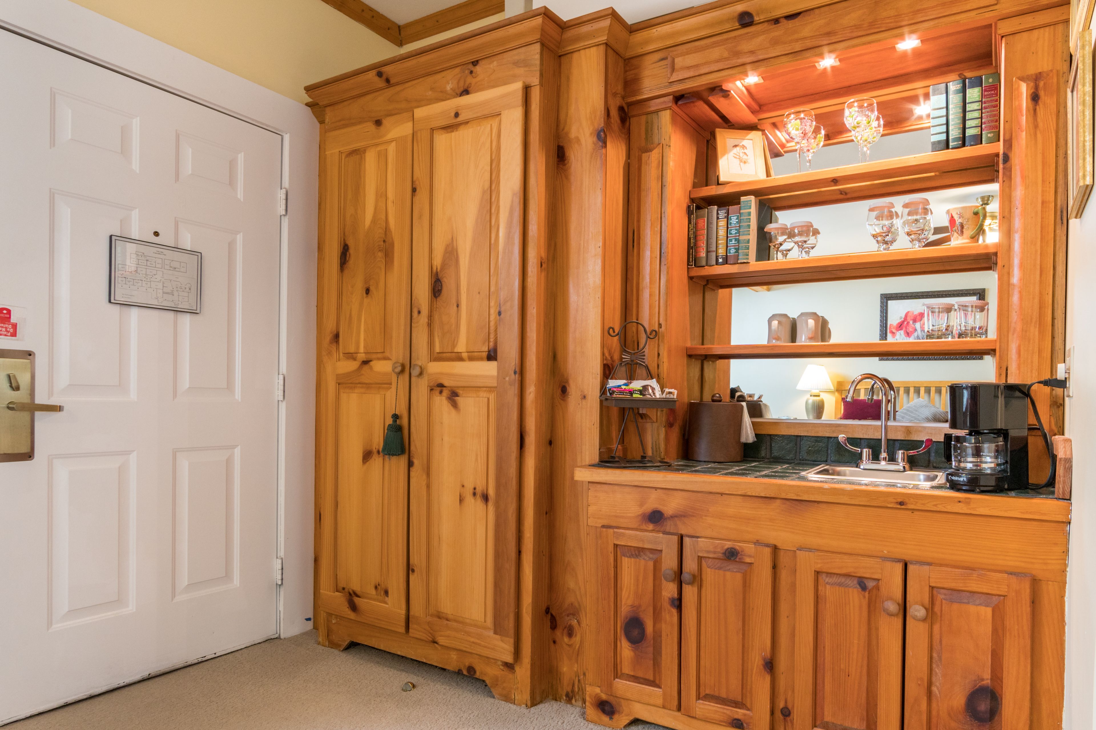 Una cocina de madera con una estantería empotrada, una cafetera y un lavamanos pequeño.