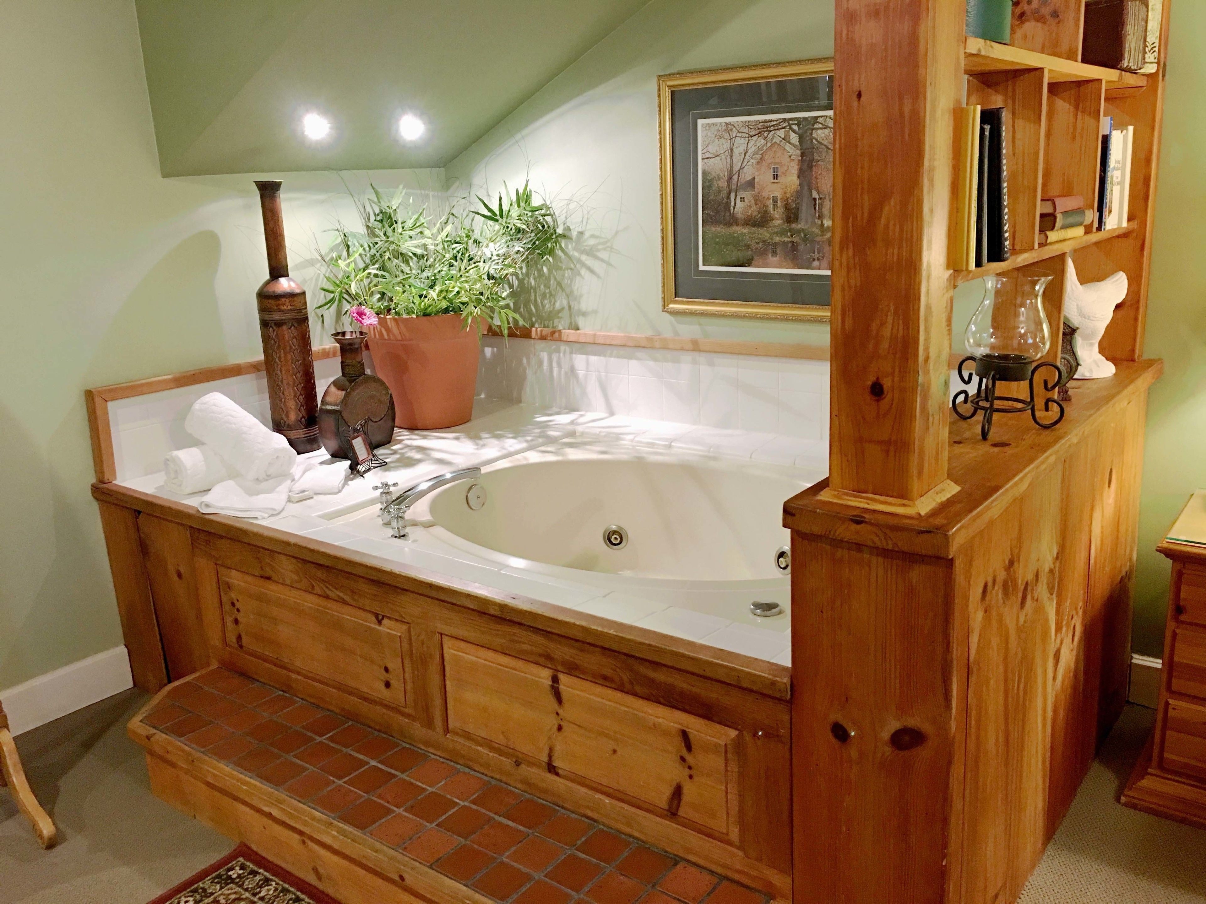 A wooden bathtub with a wooden bench, a potted plant, and a framed picture on the wall.