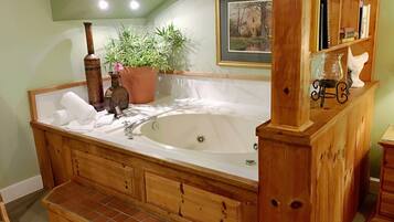 A wooden bathtub with a wooden bench, a potted plant, and a framed picture on the wall.