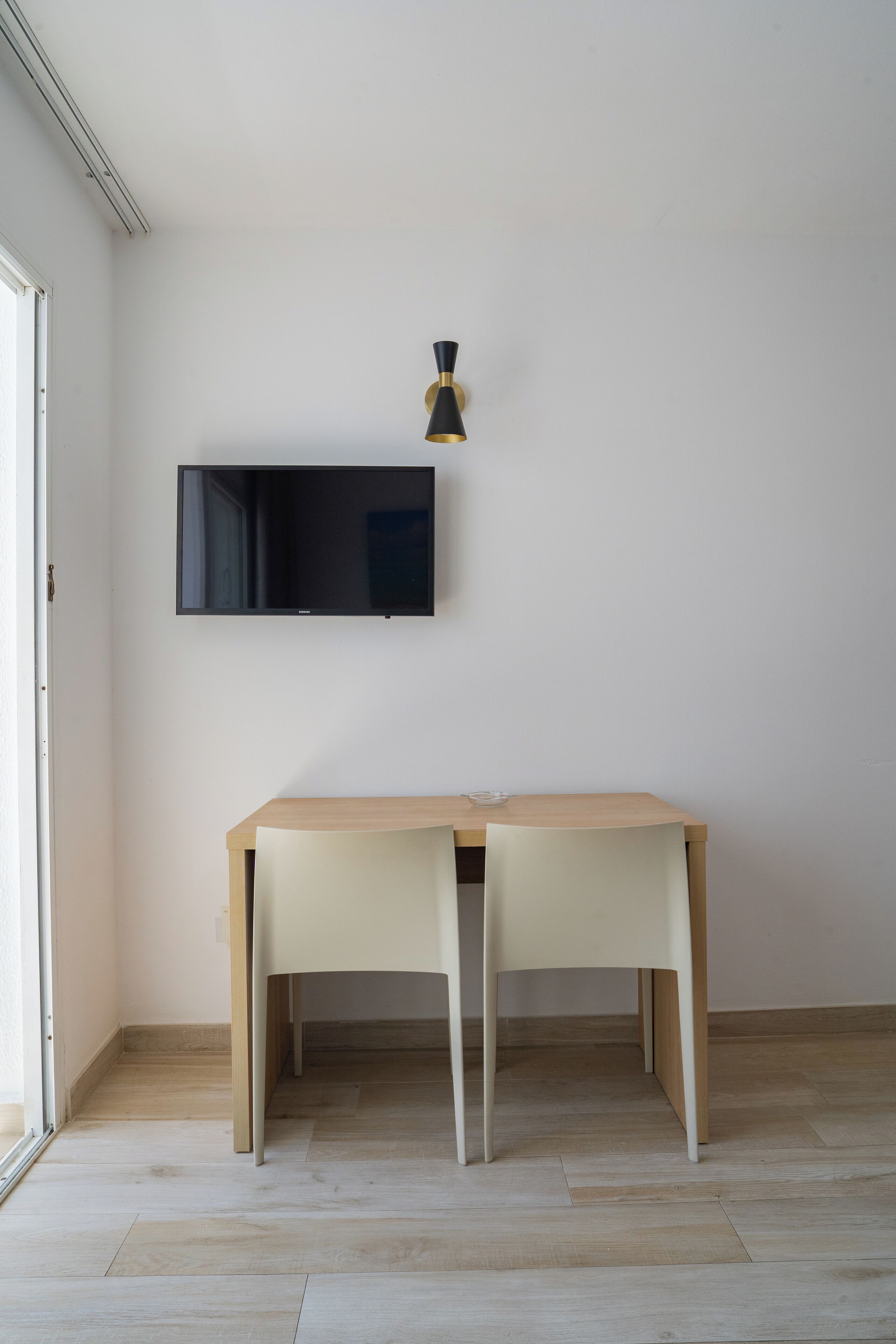A room with a flat-screen TV mounted on the wall, a wooden table with chairs, and a light fixture above the table.