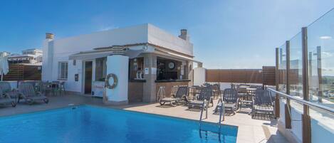 A rooftop pool with lounge chairs and a bar area.