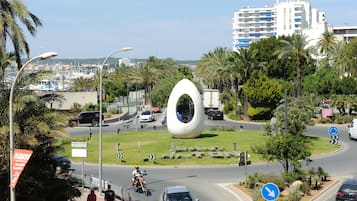 A roundabout with a distinctive white sculpture, palm trees, and a modern building in the background.