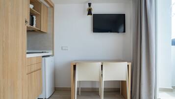 Una cocina compacta con microondas integrado, un refrigerador pequeño y un mueble de madera. Un televisor de pantalla plana está montado en la pared sobre una mesa de comedor de madera con dos sillas.