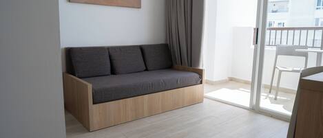 Una sala de estar moderna con un sofá de madera, un cuadro de una playa y vistas a un balcón con una silla.