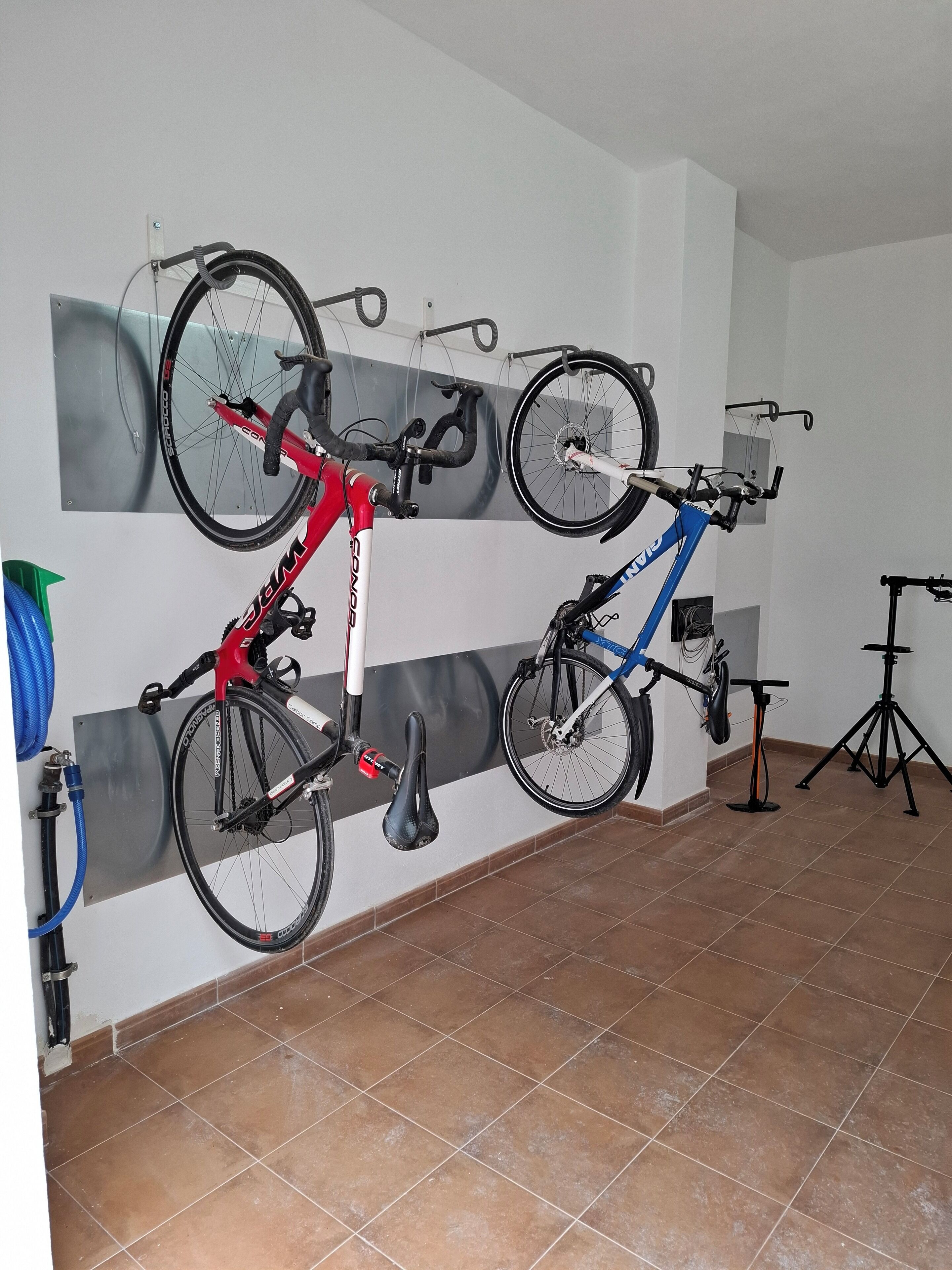 A room with a tiled floor, a wall-mounted bike rack holding three bicycles, and a tripod stand in the corner.