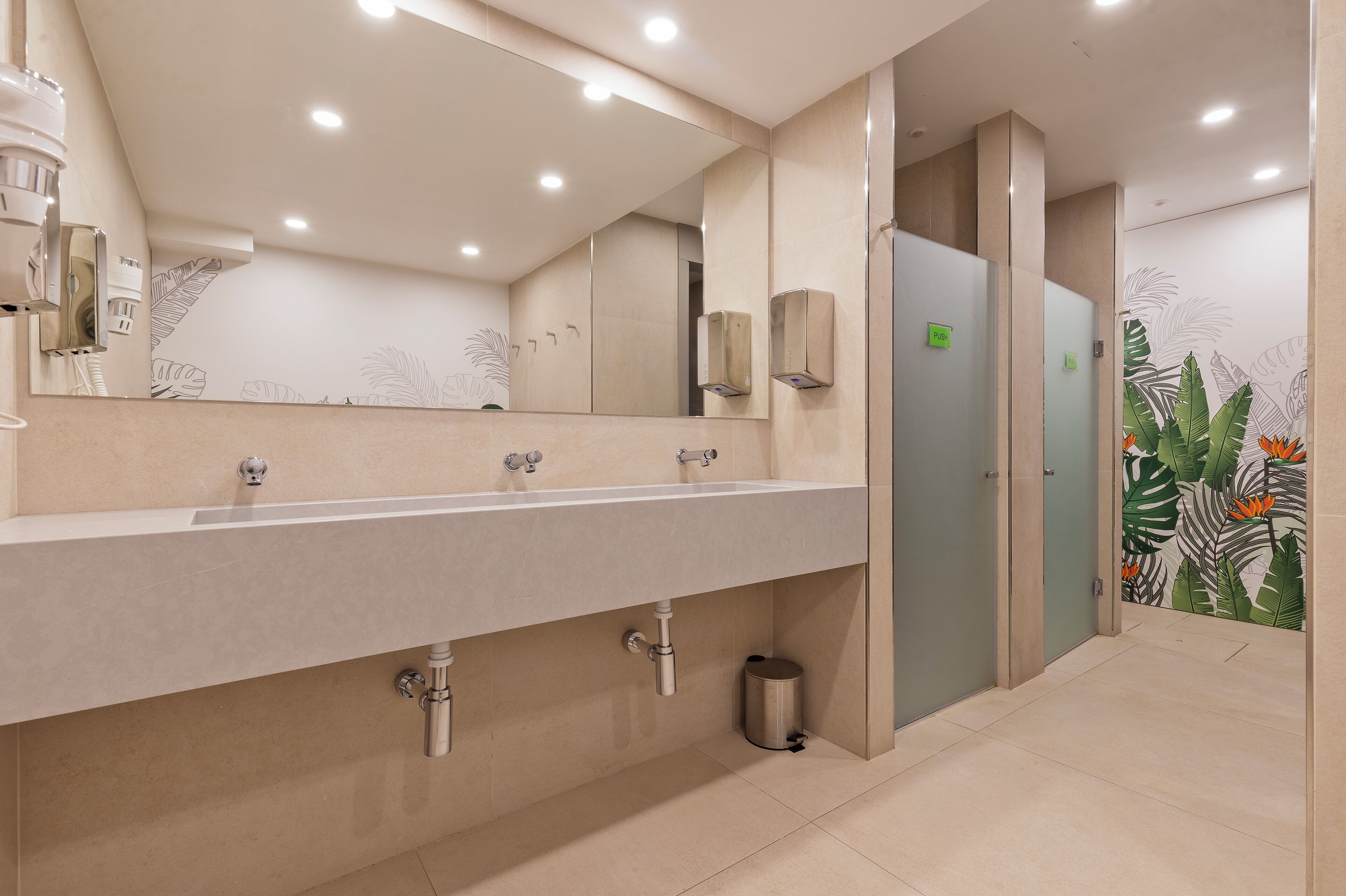 Une salle de bain moderne avec un grand miroir, plusieurs lavabos et une poubelle.