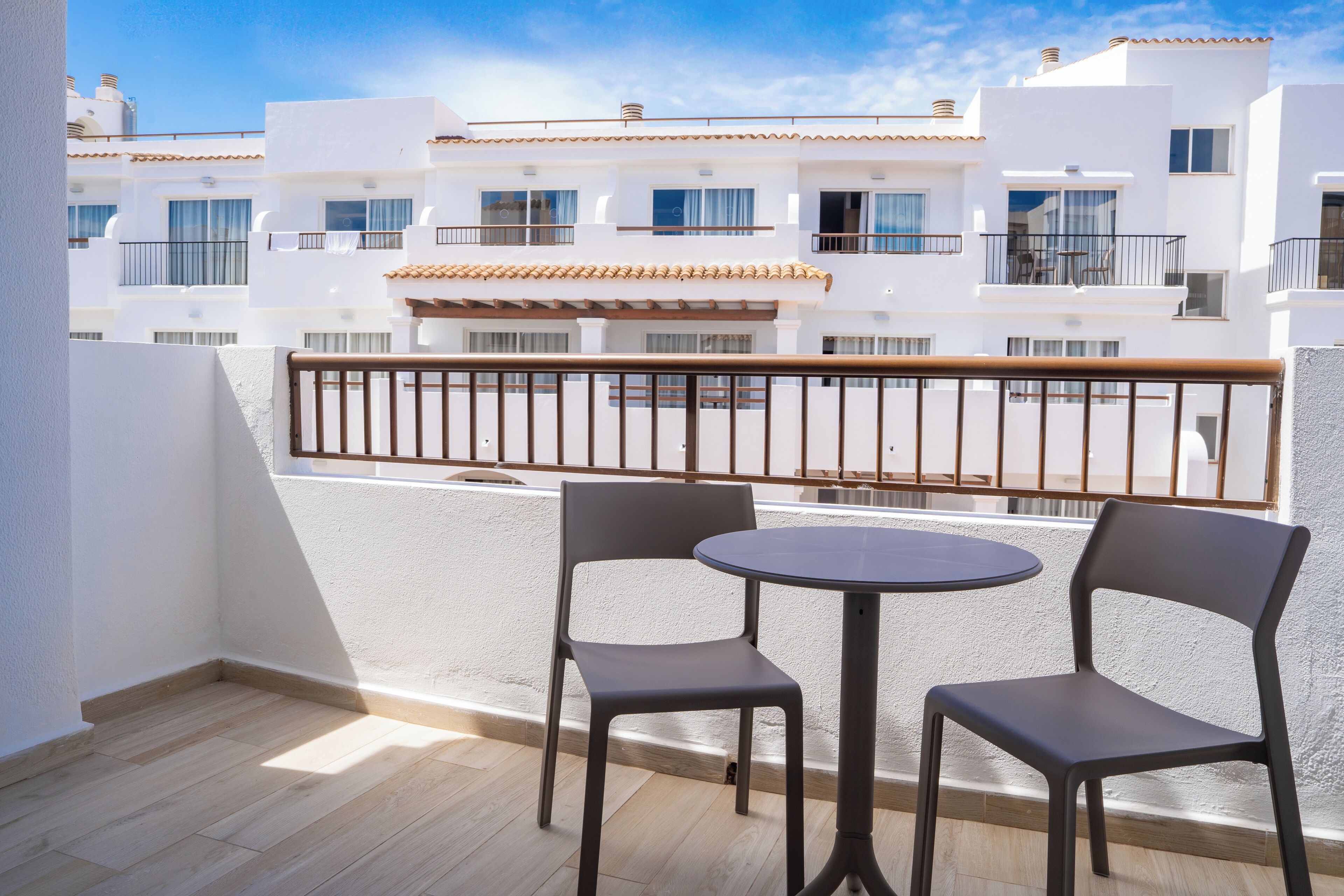 Un balcón con dos sillas y una mesita pequeña, con vistas a un edificio blanco con balcones.