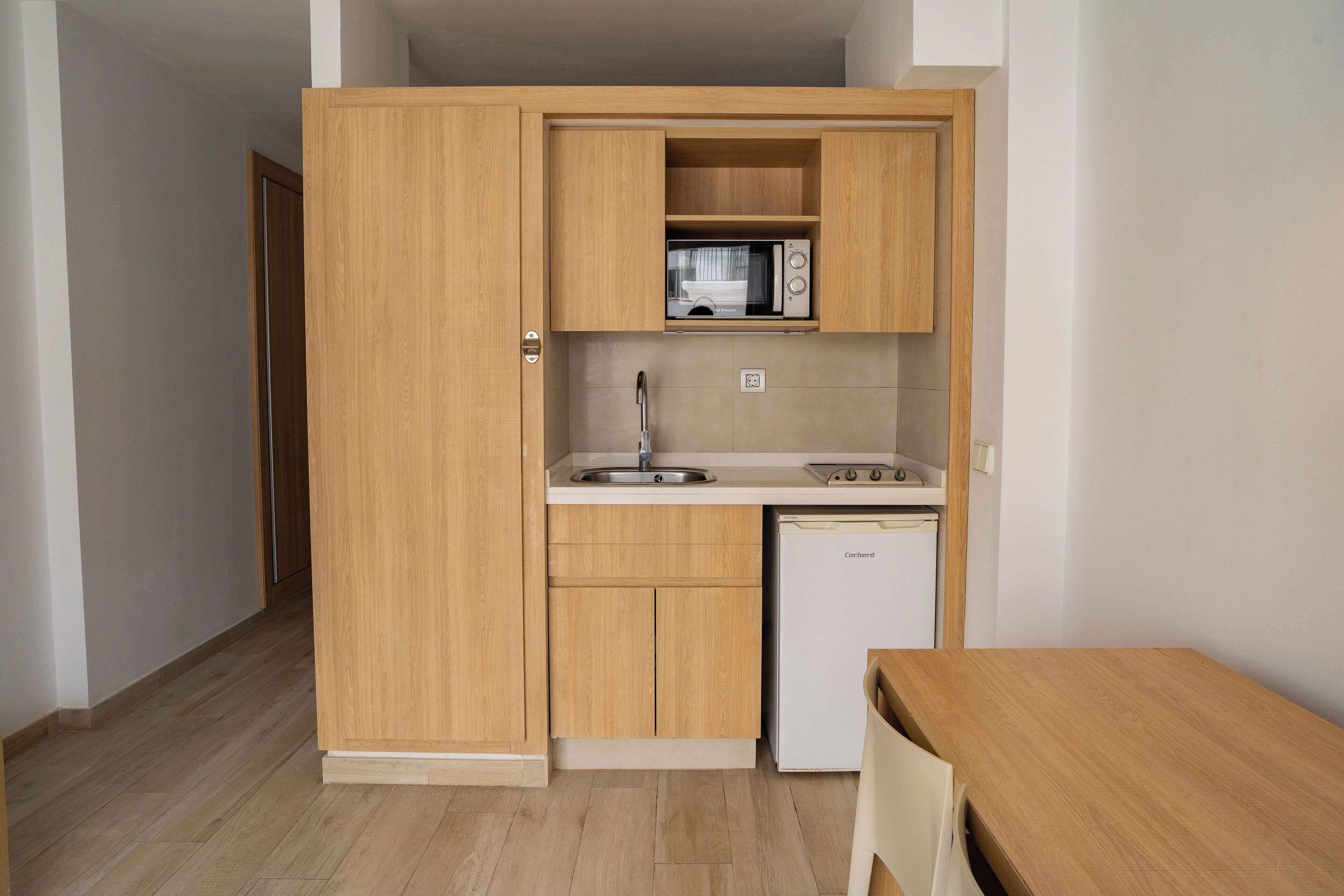 A compact kitchen with wooden cabinets, a microwave, a sink, and a dishwasher.