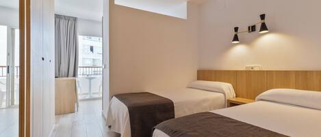 Habitación de hotel con dos camas, cabecero de madera, mesita de noche y lámpara de pared.