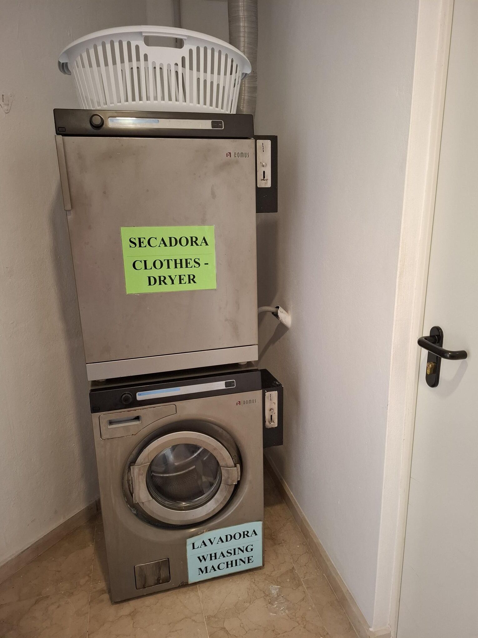 A washing machine and dryer stacked in a laundry room with a door and a wall-mounted basket.