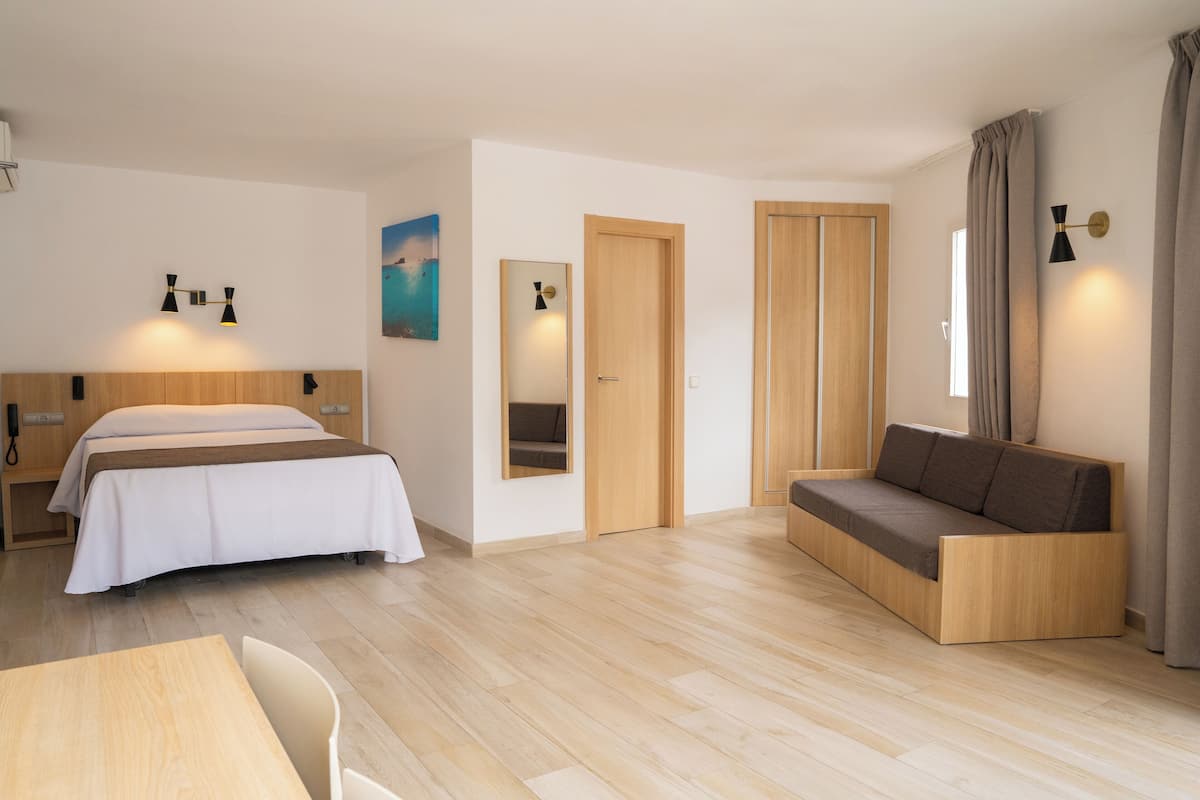 A modern hotel room with a bed, a sofa, a desk, and a mirror.