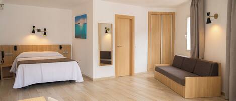 A modern hotel room with a bed, a sofa, a desk, and a mirror.