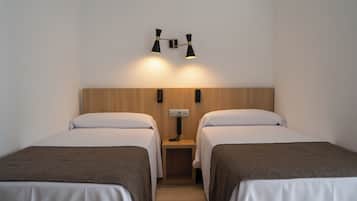 Una habitación de hotel con dos camas individuales, un cabecero de madera, una mesita de noche con lámpara y un aplique de pared.