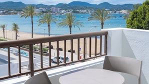 A balcony with a round table and two chairs, overlooking a beach with palm trees and boats. - Sunside Ibiza Studios - Adults Only (Sant Antoni de Portmany)