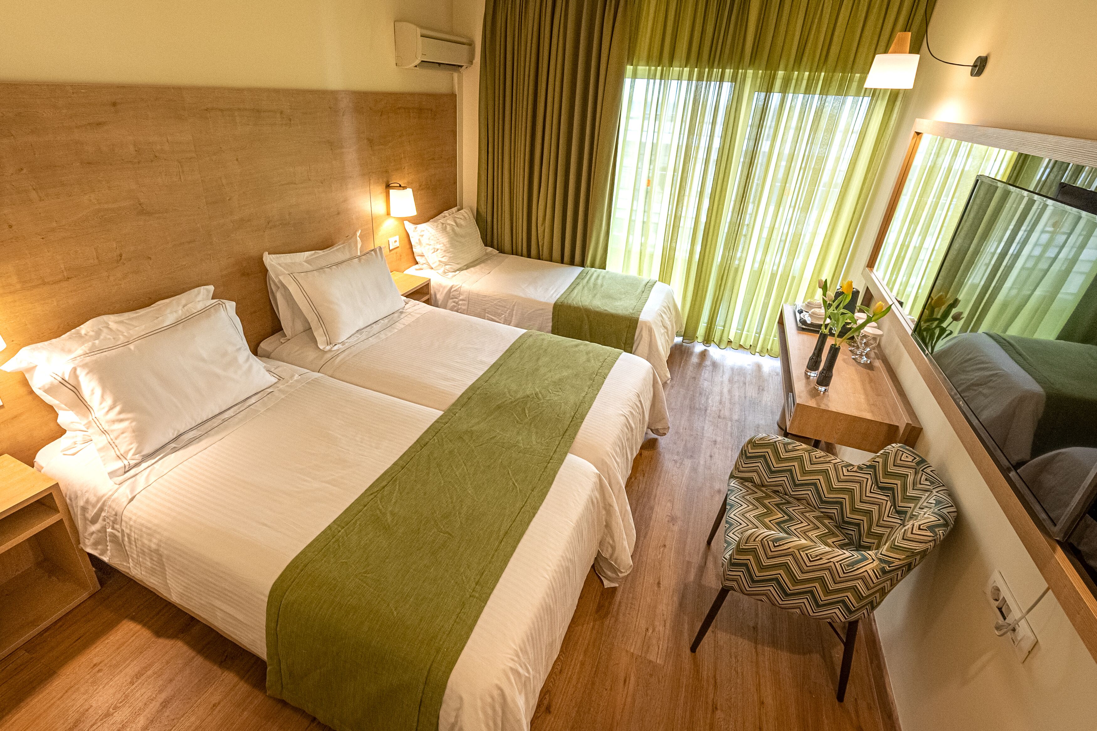 Une chambre d’hôtel avec deux lits, une petite table sur laquelle se trouve un vase, une chaise et un miroir.