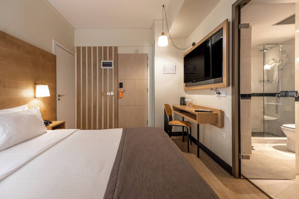 A hotel room with a bed, desk, chair, TV, and shower area.