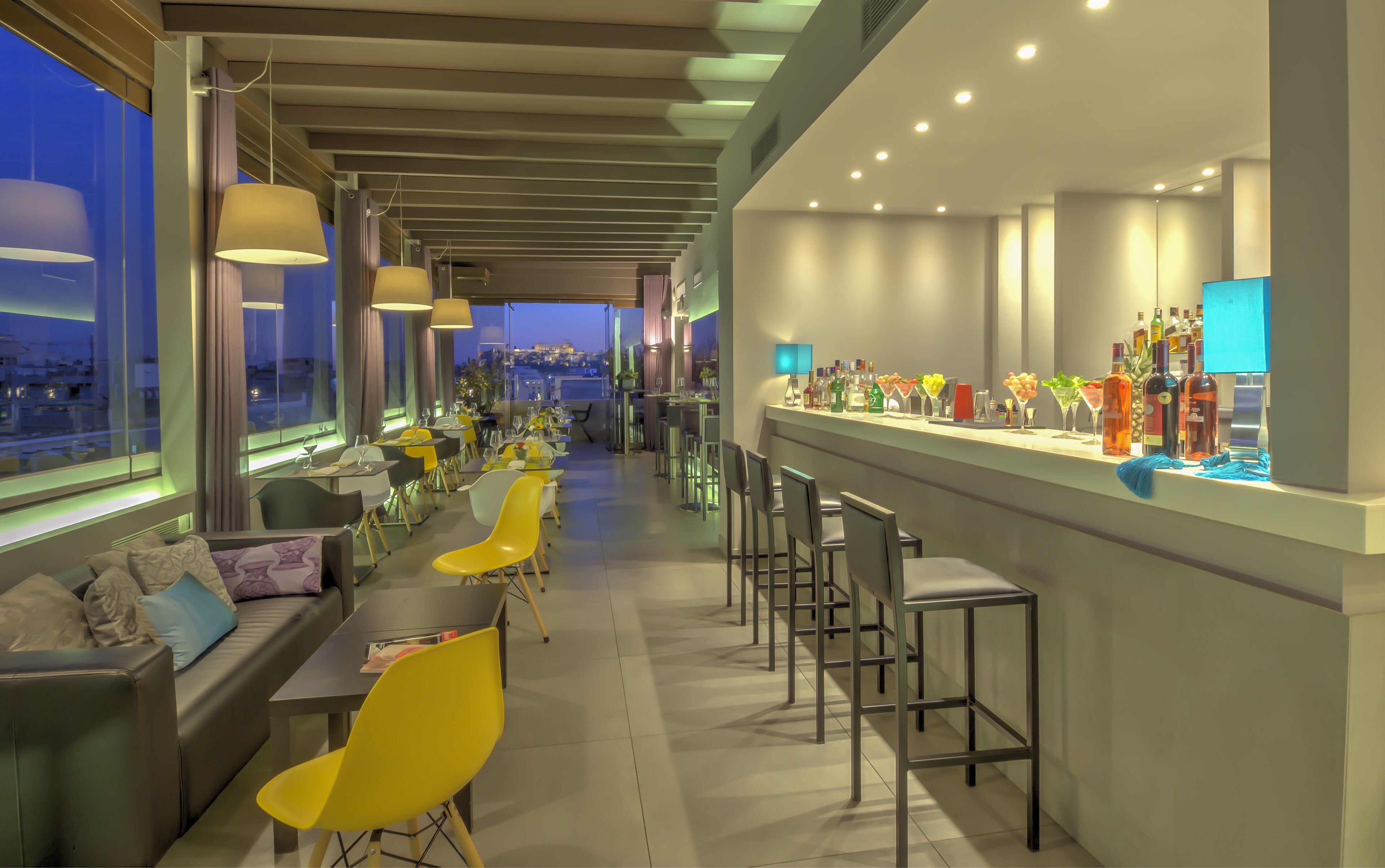 A modern bar area with seating and a view of the cityscape at dusk.