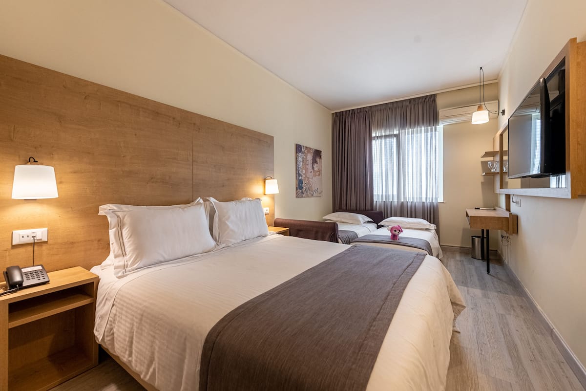 A hotel room with a large bed, bedside lamps, a desk with a flat-screen TV, and a window with curtains.