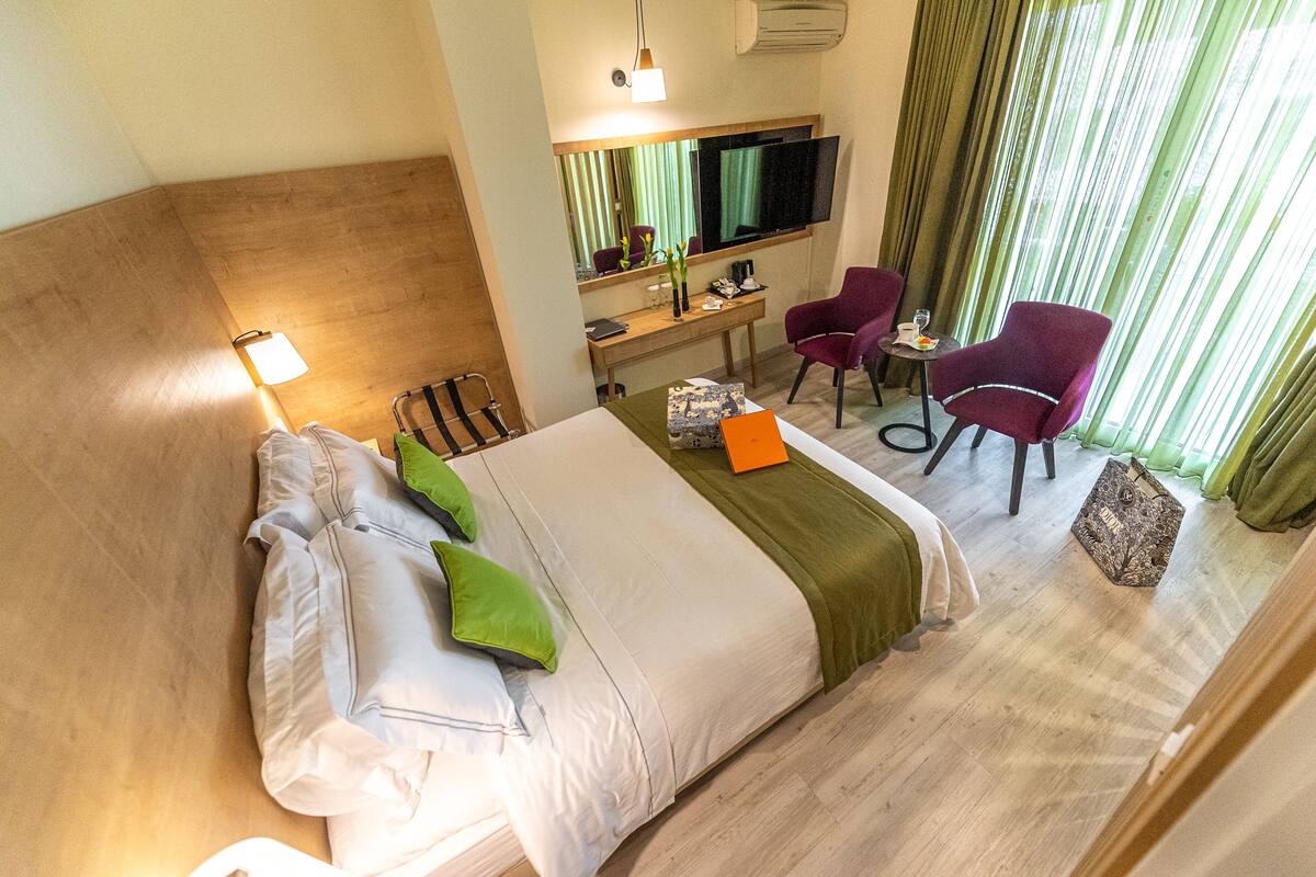 A hotel room with a large bed, a desk, two chairs, a TV, and a window with curtains.