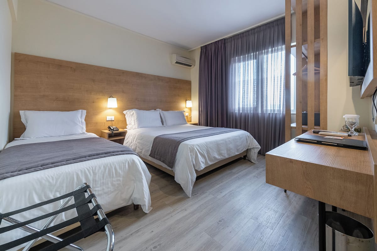 A hotel room with two beds, a desk, a chair, a TV, and a window with curtains.