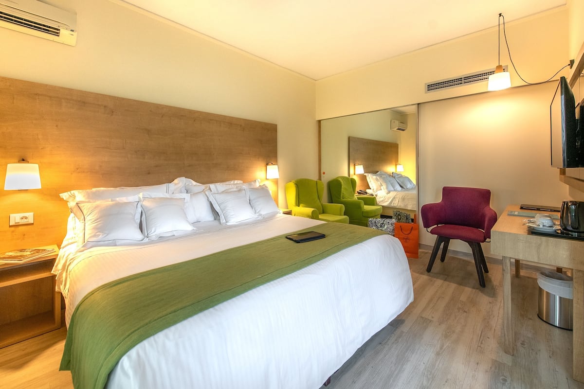 A hotel room with a large bed, a desk, a chair, and a mirror.