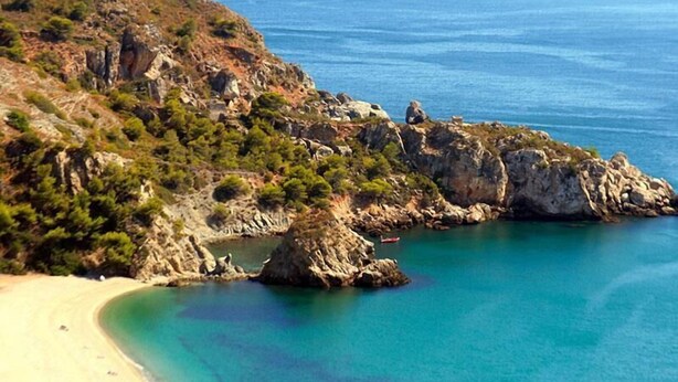 Un paysage côtier caractérisé par un terrain rocheux, une mer bleue et limpide, et une plage de sable.