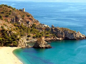 A coastal landscape with rocky terrain, a clear blue sea, and a sandy beach. - Hotel Perla Marina (Nerja)