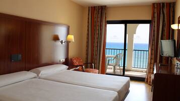 Habitación de hotel con dos camas, televisión, escritorio, silla y balcón con vistas al mar.
