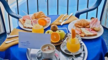 Un bufé de desayuno con croissants, jamón, huevos y fruta, dispuesto en una mesa junto a una piscina.