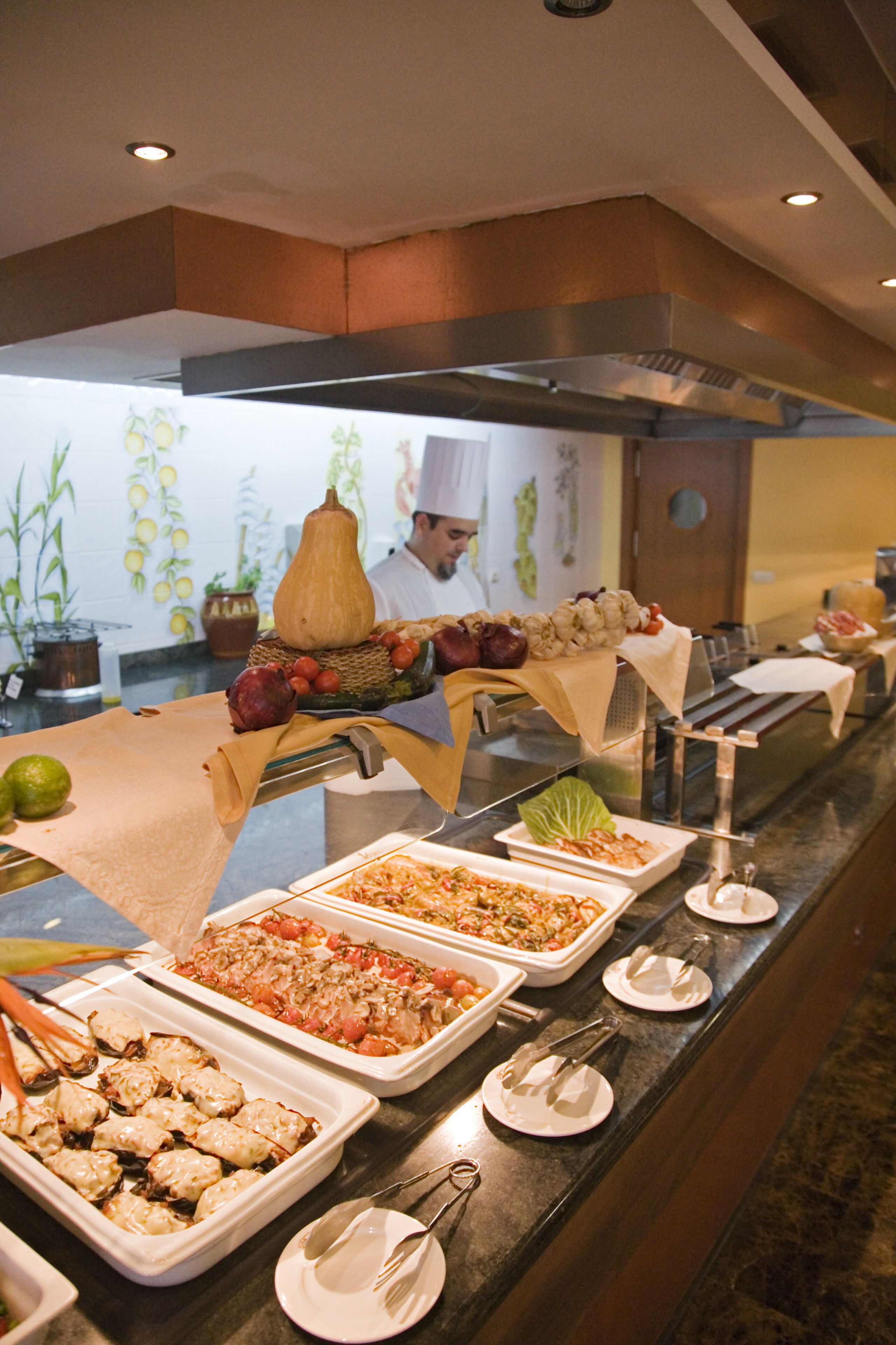 Ein Buffet mit verschiedenen Speisen, darunter eine große Kürbisdekoration, auf einer Theke mit Besteck und Tellern angerichtet.