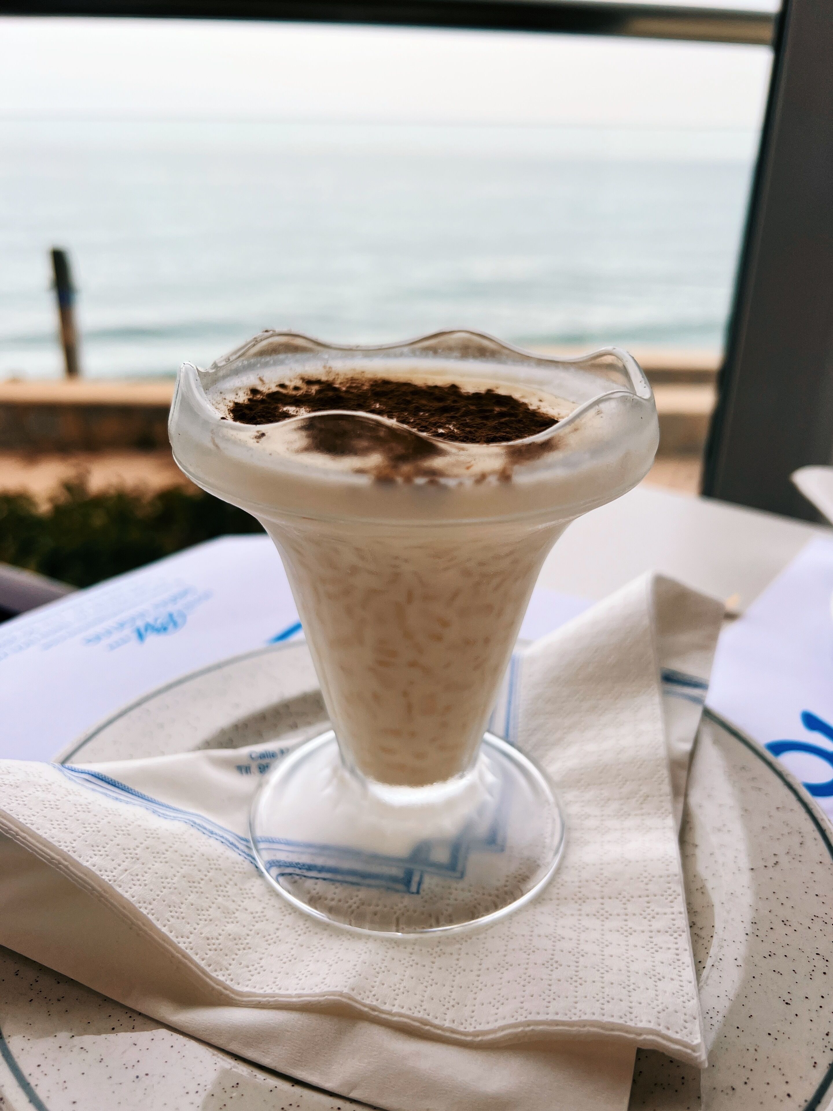 Un postre en un vaso sobre una mesa, con vista al mar.