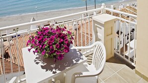 Un balcon avec une table et des chaises, donnant sur une plage bordée de palmiers et sur l’océan.