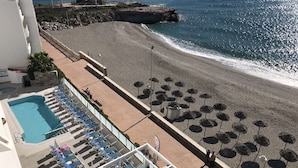 Un hôtel situé en bord de mer, doté d’une piscine, de chaises longues, de parasols et bordé d’une côte rocheuse.